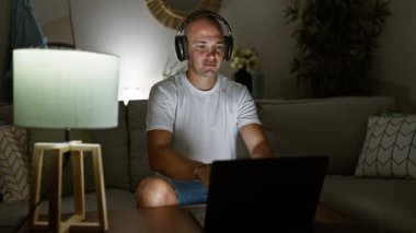 Genç İspanyol adam evde kanepede oturmuş müzik dinliyor.