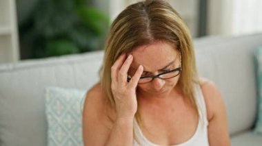 Orta yaşlı İspanyol kadın evinde ciddi bir ifadeyle kanepede oturuyor.