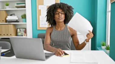 Afrika kökenli Amerikalı iş kadını bilgisayarını ofiste el fanı olarak kullanıyor.