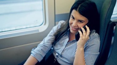 Genç ve güzel İspanyol kadın gülümsüyor. Telefonda konuşuyor. Tren vagonunda oturuyor.