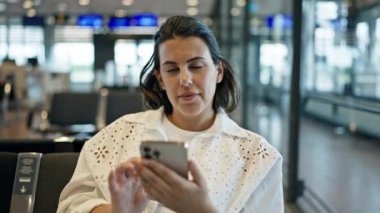 Havaalanında gülümseyen akıllı telefon kullanan güzel bir İspanyol kadın.