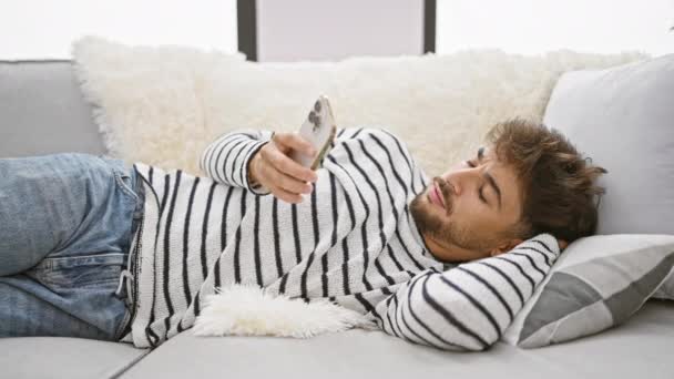 精疲力尽的年轻人一边用智能手机发短信 一边打呵欠 在家里舒适的沙发上睡着了 — 图库视频影像