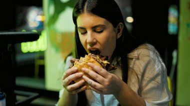 Genç ve güzel İspanyol kadın restoranda lezzetli hamburgerler yiyor.