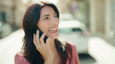 Orta yaşlı İspanyol kadın gülümsüyor. Akıllı telefondan konuşuyor.