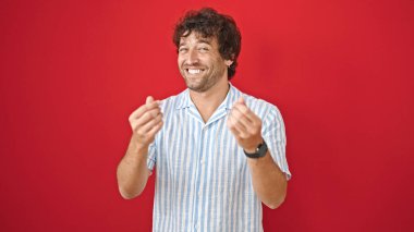 Genç İspanyol sırıtan, kendine güvenen, soyutlanmış kırmızı arka planda para hareketi yapan