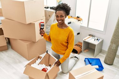 Afro-Amerikalı kadın yeni evinde kendine güvenen bir karton kutu paketliyor.