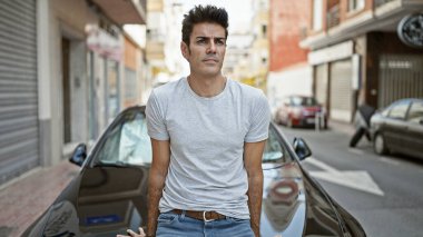 Sokakta yüzü ciddi bir şekilde oturan Latin asıllı genç bir adam.