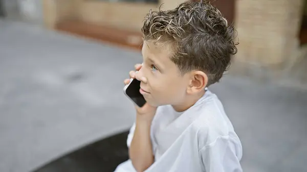 Adorável Menino Loiro Absorvido Conversa Telefônica Séria Sentado Banco Cidade — Fotografia de Stock