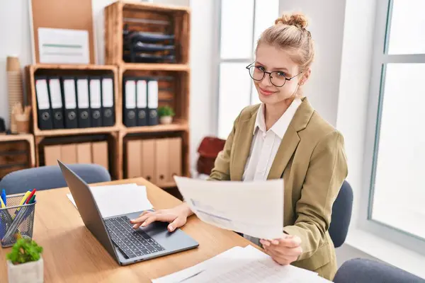 Young blonde woman business worker using laptop reading document at office