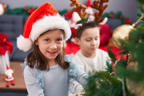 可爱的男孩和女孩在家里装饰圣诞树 免版税图库照片