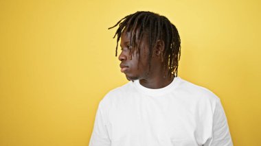 İzole edilmiş sarı arka plan üzerinde ciddi bir ifadeyle duran Afrikalı Amerikalı adam.