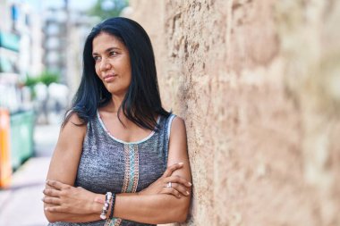 Orta yaşlı İspanyol kadın caddede kollarını kavuşturup el kol hareketi yapıyor.