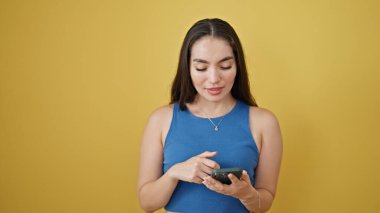 Akıllı telefon kullanan genç, güzel İspanyol kadın izole edilmiş sarı arka planda gülümsüyor.