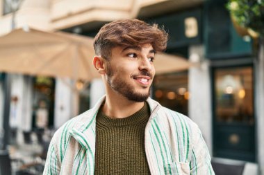 Genç Arap adam gülümsüyor. Kendinden emin. Caddenin kenarına bakıyor.