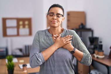 Ofiste çalışan Afrikalı Amerikalı bir kadın gözlük takıyor elleri göğsünde, gözleri kapalı gülümsüyor ve yüzünde minnet ifadesi var. sağlık kavramı. 