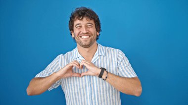 Genç İspanyol adam gülümsüyor. Kendine güveniyor. Kalp hareketi yapıyor.