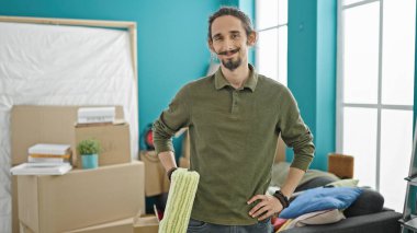 Genç İspanyol adam gülümsüyor. Yeni evinde boya silindiri tutuyor.