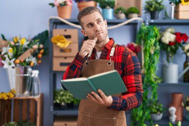 Young caucasian man florist reading notebook with doubt expression at flower shop