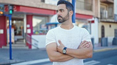 Genç İspanyol adam ciddi bir ifadeyle ve caddede çapraz hareketlerle yan tarafa bakıyor.