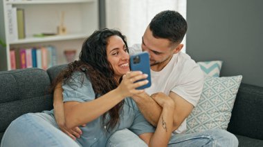 Kadın ve erkek akıllı telefon kullanıyor. Kanepede oturuyor ve gülümsüyor.