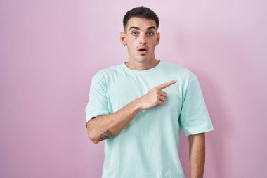 Pembe arka planda duran yakışıklı İspanyol adam parmağını yana doğru kaldırarak şaşırdı, ağzı açık hayret içinde kaldı.. 