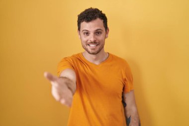 Sarı arka planda duran genç İspanyol adam gülümsüyor. Avuç içi dolusu yardım ve kabullenme teklif ediyor.. 