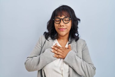 Tecrit edilmiş arka planda duran İspanyol kadın elleri göğsünde, gözleri kapalı ve yüzünde minnet dolu bir jest ile gülümsüyor. sağlık kavramı. 