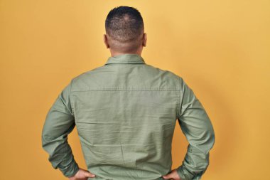 Sarı arka planda duran İspanyol genç adam geriye doğru bakıyor kolları vücudunda. 