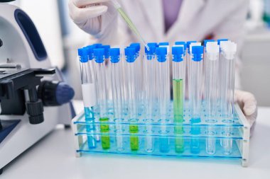 Genç beyaz kadın bilim adamı laboratuardaki test tüplerine sıvı döküyor.