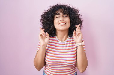 Orta Doğulu genç bir kadın pembe arka planda duruyor. Umut ve gözlerin kapalı gülümseyerek işaret ediyor. Şans ve batıl inançlar. 