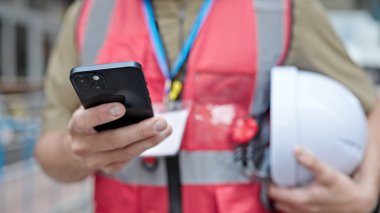 Kafkasyalı genç bir mimar inşaat alanında akıllı telefon kullanıyor.