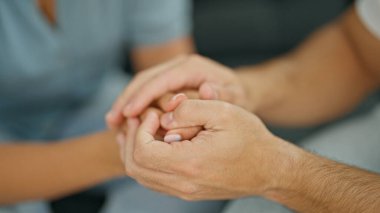 Kanepede oturan erkek ve kadın çiftin elleri birbirine kenetlenmiş.