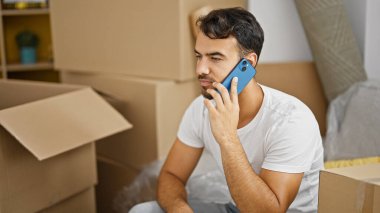 Genç İspanyol adam akıllı telefondan konuşuyor. Yeni evindeki kanepede oturuyor.