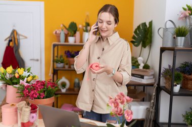 Çiçekçide elinde dantelle akıllı telefondan konuşan beyaz kadın çiçekçi.