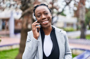 Afro-Amerikalı kadın gülümsüyor. Parktaki akıllı telefondan konuşuyor.