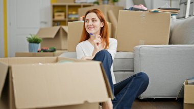 Genç kızıl saçlı kadın yerde oturuyor ve yeni evini düşünüyor.