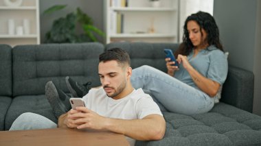 Man and woman couple using smartphone sitting on sofa at home