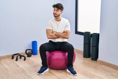 Sakallı İspanyol bir adam yoga odasında pilatese oturmuş gülümsüyor ve başka tarafa bakıyor.. 