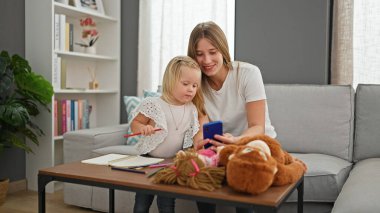 Oturma odasındaki kanepede rahat rahat oturmuş, dijital dünyalarına dalarken, akıllı telefon ekranlarına bakarken birlikte gülümseyen beyaz anne ve kızlarıyla evde iç açıcı bir sahne..