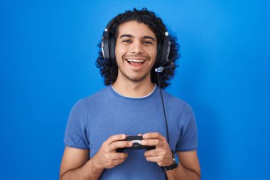 Kıvırcık saçlı İspanyol adam video oyunu oynuyor. Kumandayı tutuyor ve kahkahalarla gülüyor.. 