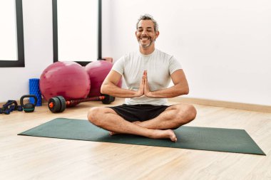 Orta yaşlı, gri saçlı, gülümseyen, spor merkezinde yoga eğitimi alan bir adam.