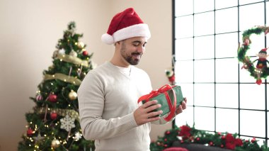 Evdeki Noel ağacının yanındaki koltukta oturan İspanyol genç adam hediyesini tutuyor.