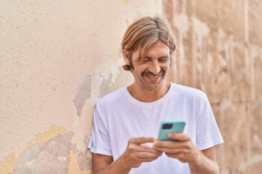Sokakta akıllı telefon kullanan, kendine güvenen genç sarışın adam.