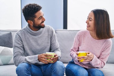 Man and woman couple sitting on sofa drinking coffee at home