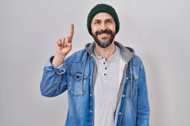 Yün şapkalı, İspanyol asıllı genç bir adam bir numaralı parmağını gösterip gülümserken kendinden emin ve mutlu.. 