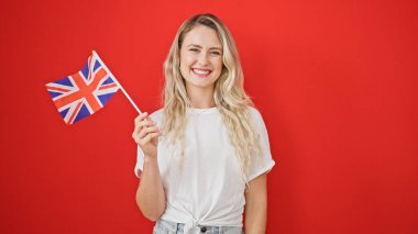 Genç sarışın kadın gülümsüyor. Birleşik krallık bayrağını izole edilmiş kırmızı arka planda tutuyor.