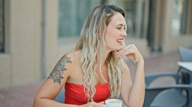 Kahve içen genç sarışın kadın kahve dükkanının terasında gülümsüyor.