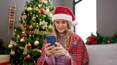 Genç sarışın kadın Noel 'i evde akıllı telefon kullanarak kutluyor.