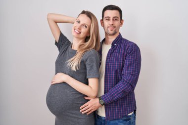 Genç bir çift beyaz arka planda duran bir bebek bekliyor gülümseyen, el hareketleriyle saçlara dokunan, çekici ve modaya uygun bir poz veren. 