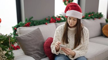 Evdeki Noel ağacının yanında akıllı telefon kullanan genç ve güzel İspanyol kadın.